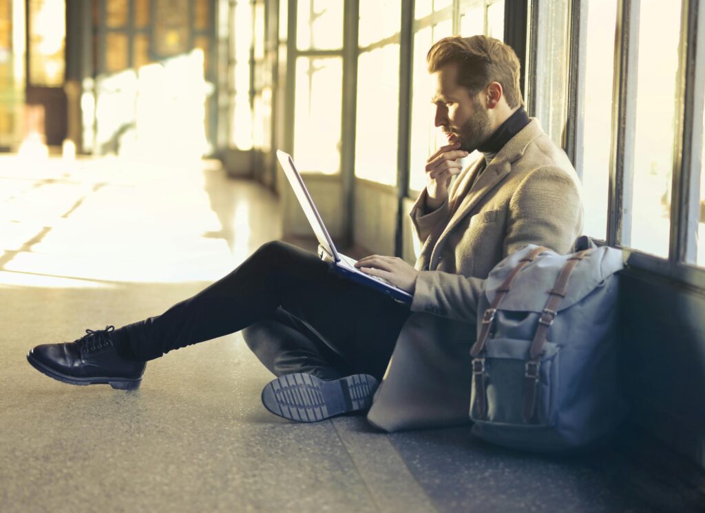 Man sitting in a hallway, squinting in confusion at his laptop propped on his lap.